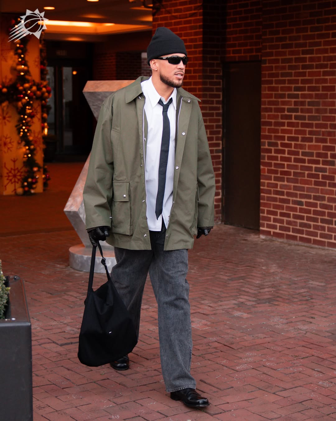 Devin Booker wearing Our Legacy Hunter jacket pine green technical panama, Our Legacy Grey wide-leg jeans and Lemaire Anatomic slip on in leather shiny black.